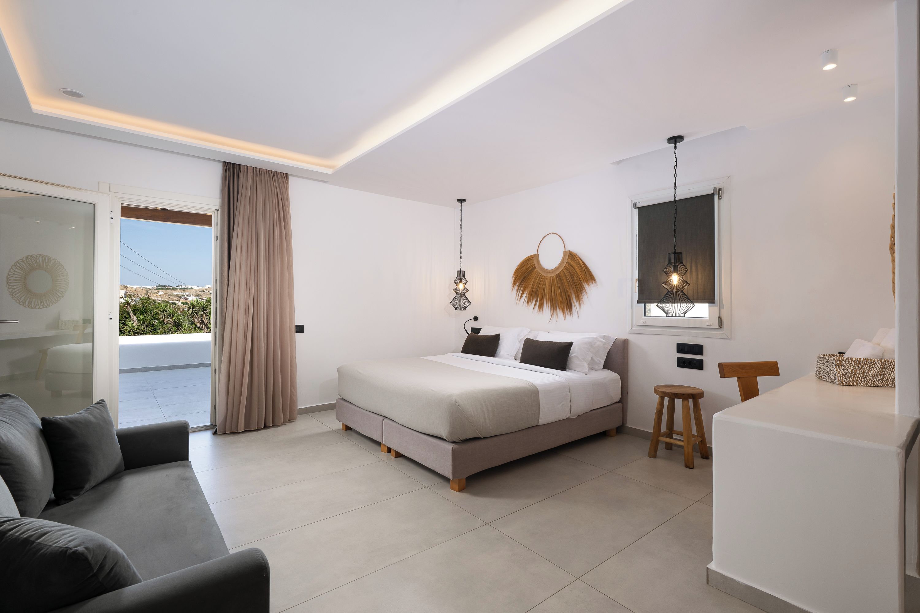 Un dormitorio moderno con cama, sofá, un taburete pequeño, escritorio y vistas a través de un ventanal.