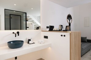 Un baño moderno con un espejo grande, un lavamanos azul, una cafetera y una escultura decorativa de un árbol.