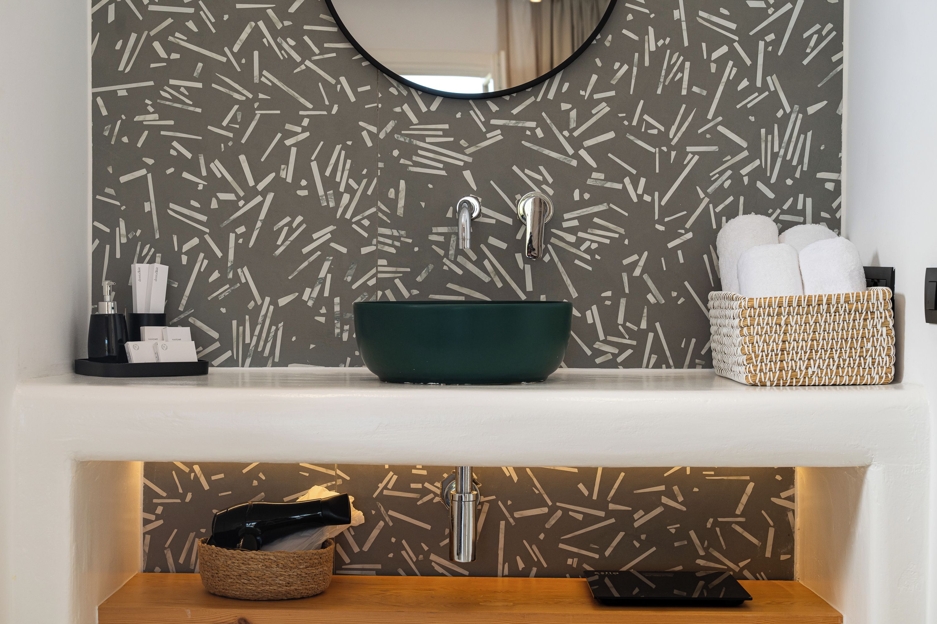 A modern bathroom with a green sink, a mirror, and a patterned wall.