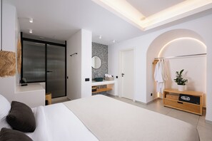 A modern bedroom with a large bed, a walk-in closet, a vanity with a mirror, and a wooden console table.