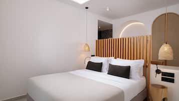 A modern hotel room with a large bed, a wooden headboard, a small wooden side table, and a wall-mounted lamp.