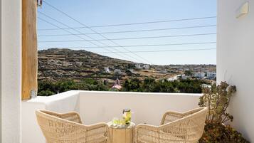 A balcony with wicker chairs, a small table, and a view of a hilly landscape.