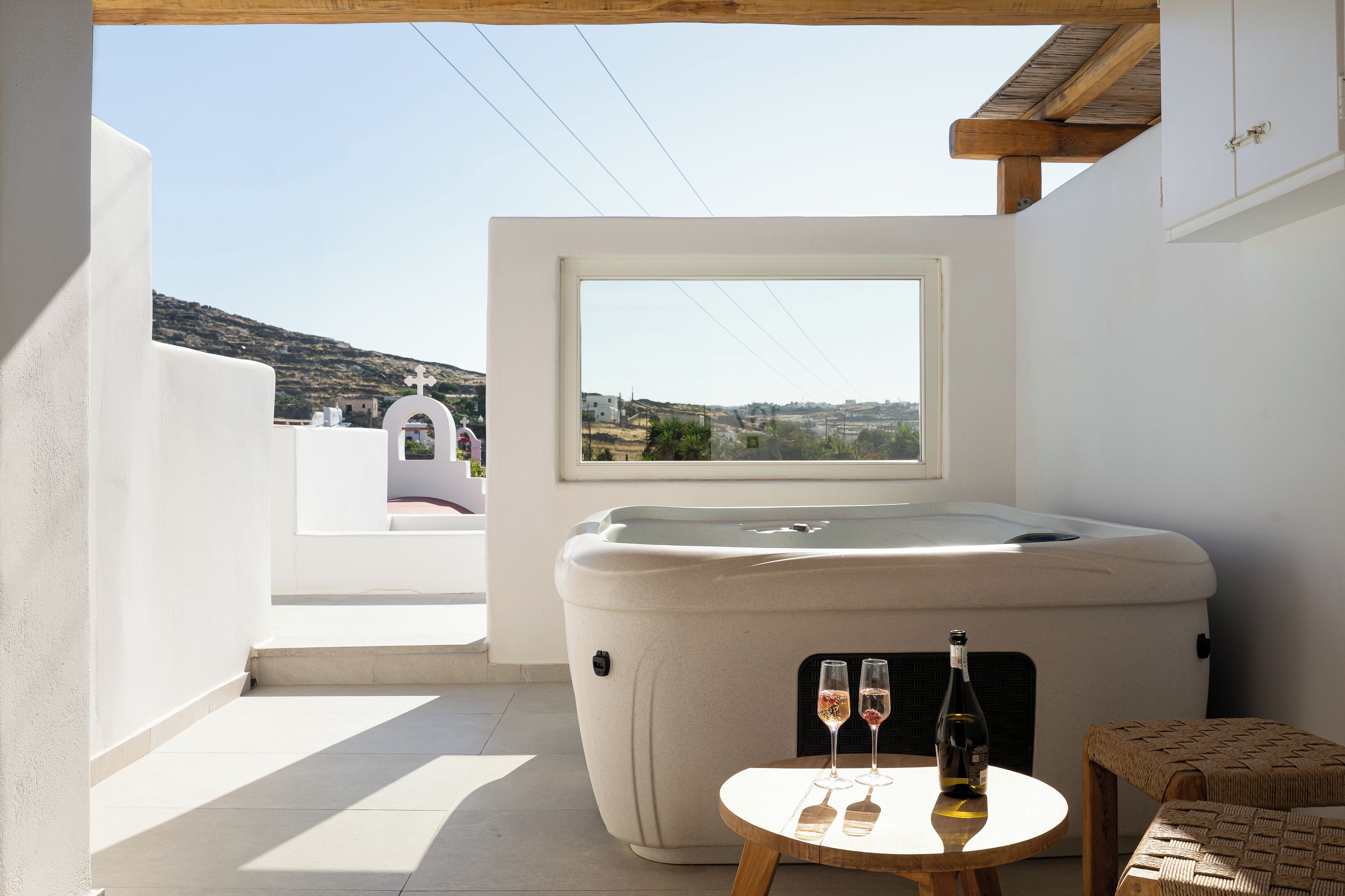 Un jacuzzi con vistas al campo, una pequeña mesa con dos copas de vino y una silla de mimbre.