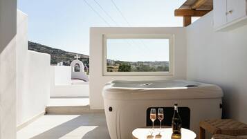 Un jacuzzi con vistas al campo, una pequeña mesa con dos copas de vino y una silla de mimbre.