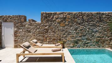 Un muro de piedra, una piscina y dos sillones de madera con toallas.