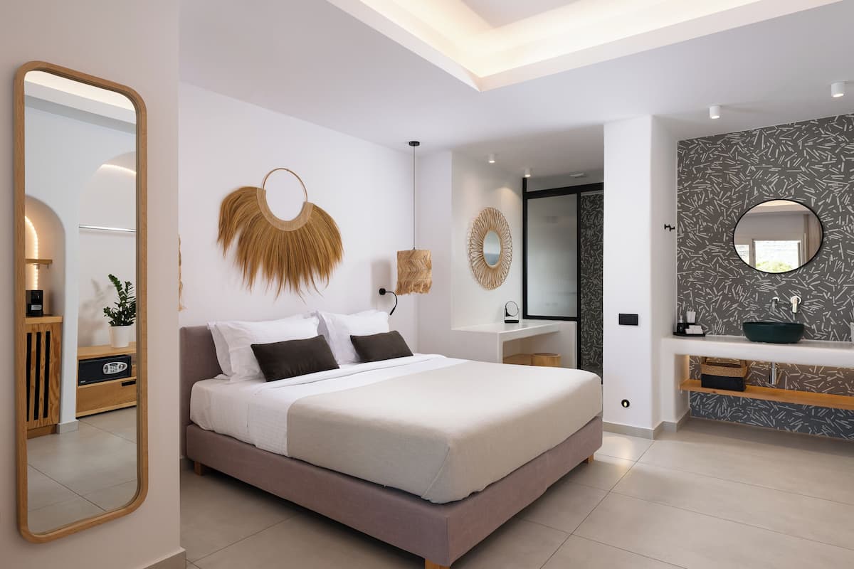 Un dormitorio moderno con una cama grande, mesitas de noche, un espejo y un baño con lavabo y espejo.