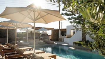 A poolside area with lounge chairs and umbrellas, a stone wall, and a modern building with a glass door.