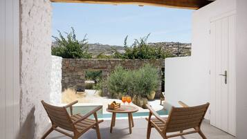 A patio with a pool, two wicker chairs, a table with drinks, and a stone wall.