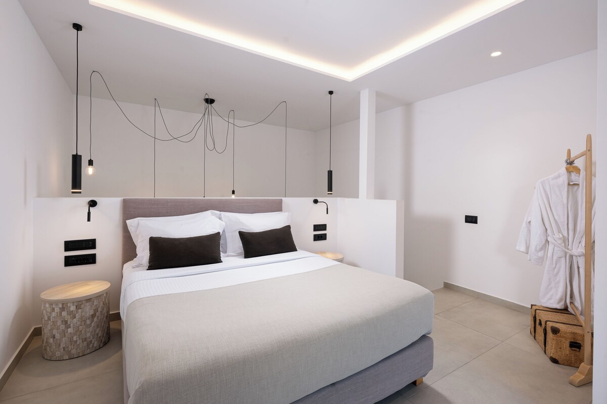 Ett modernt hotellrum med en stor säng, sängbord, ett runt sidobord, en klädställning och en taklampa.