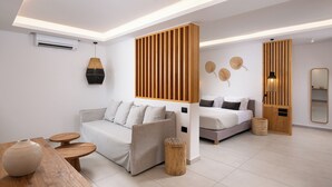 Una habitación de hotel moderna con sofá, cama, un panel de madera, un taburete de madera redondo, una lámpara trenzada y un espejo.
