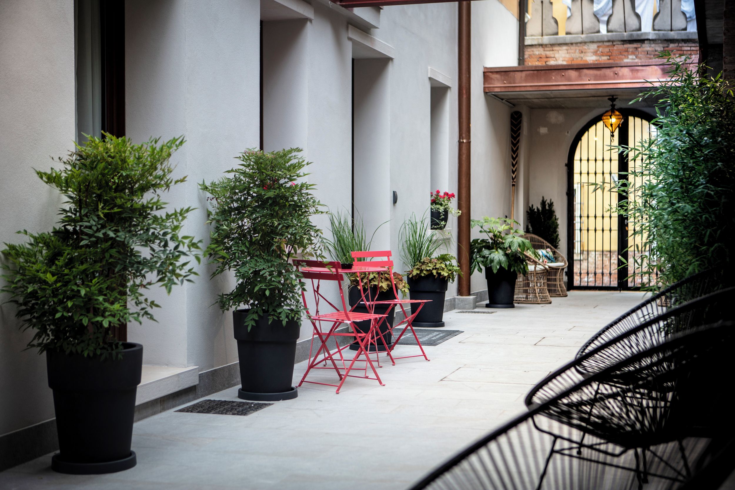 A courtyard with potted plants, red chairs, and a black chair.