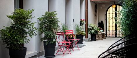 A courtyard with potted plants, red chairs, and a black chair.