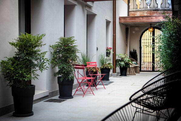 A courtyard with potted plants, red chairs, and a black chair.
