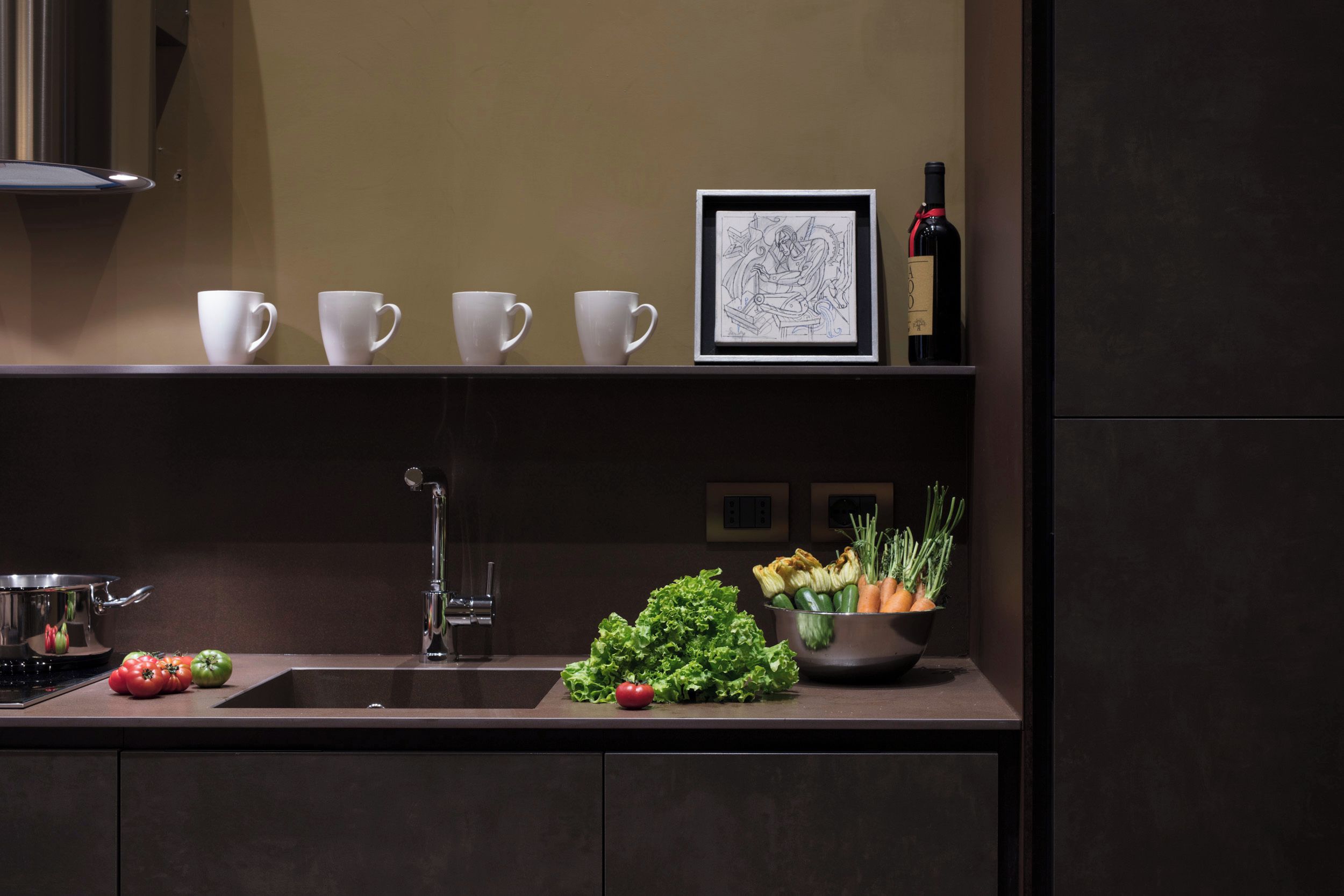 A kitchen with a sink, a framed artwork, and a bottle of wine on the counter.