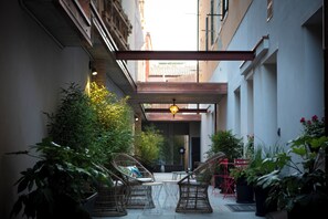 A narrow outdoor corridor with wicker furniture, potted plants, and a hanging light fixture.
