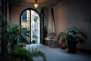 A corridor with wicker chairs, potted plants, and a view of a canal and buildings. - Aqua Apartments (Venice)