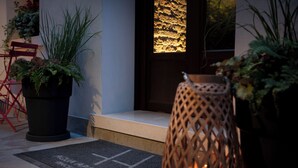 A hotel entrance with a doormat, potted plants, a wicker chair, and a textured wall. - Aqua Apartments (Venice)