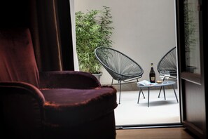 A room with a purple chair, a table with two chairs, a bottle, and a glass.