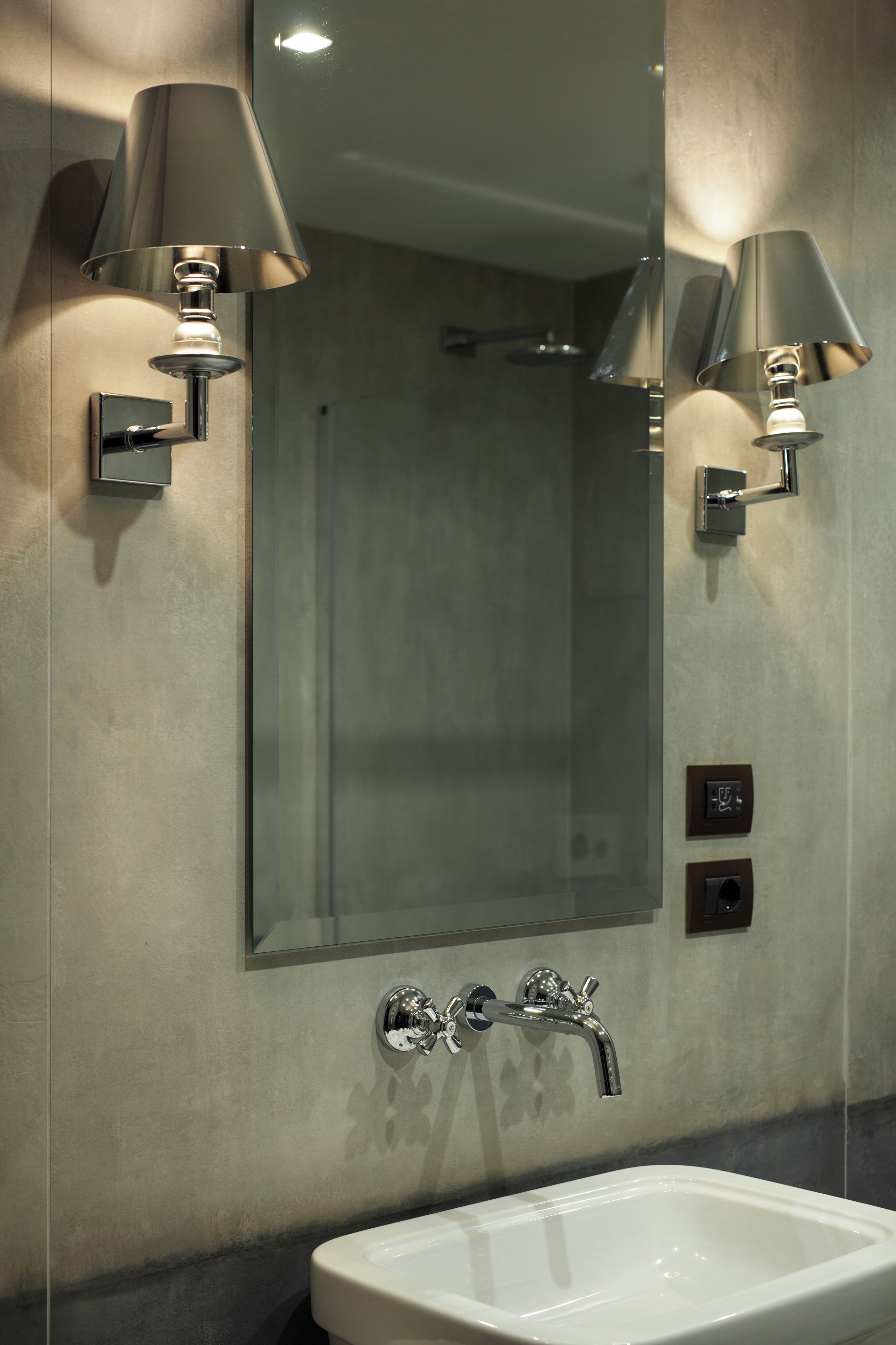 A bathroom with a large mirror, two wall-mounted lamps, a sink, and a shower.