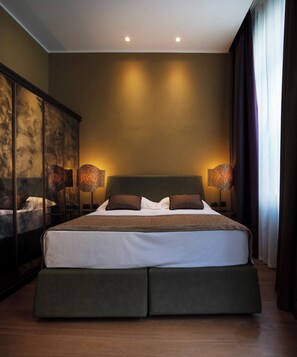 A modern bedroom with a large bed, two bedside lamps, and a large mirror on the left. - Aqua Apartments (Venice)