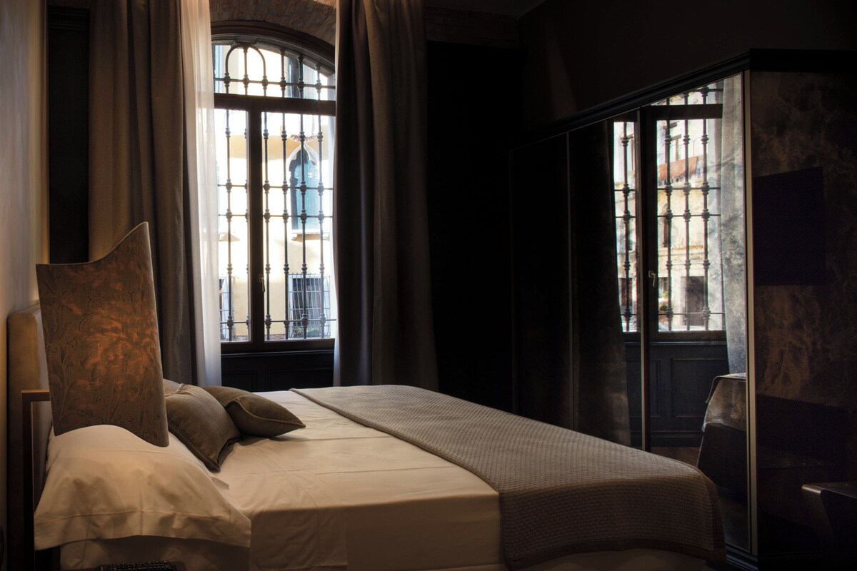 A bedroom with a bed, curtains, a window with a view, and a wardrobe.