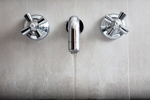 A bathroom with three chrome faucets and a visible water stream.