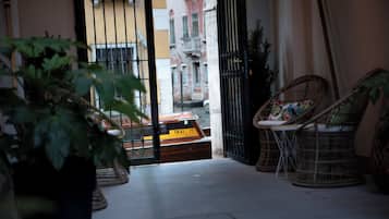 Un balcón interior con sillas de mimbre, una planta en maceta y vistas de un edificio con un letrero amarillo.