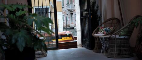 Un balcon intérieur avec des fauteuils en osier, une plante en pot et une vue sur un immeuble orné d’une enseigne jaune.
