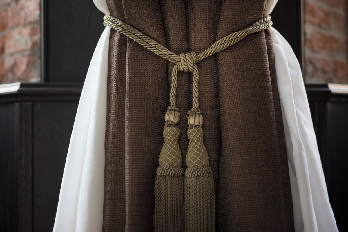 A close-up of a brown curtain with a rope tied in a knot and tassels.