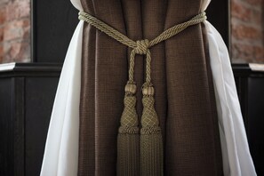 A close-up of a brown curtain with a rope tied in a knot and tassels.