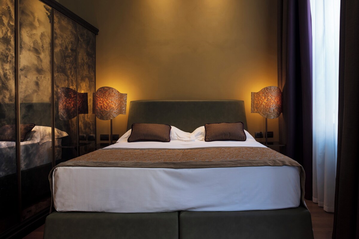 A modern bedroom with a large bed, two bedside lamps, and a large mirror on the left.