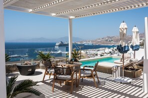 Une terrasse dotée d’une piscine, de chaises longues et de parasols, offrant une vue imprenable sur la côte et les navires de croisière.