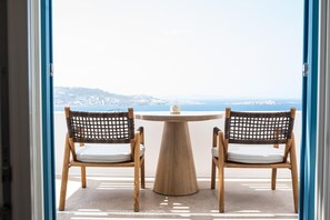A view through a door of a room with two wicker chairs and a round table, overlooking a coastal landscape. - Numi Boutique Hotel Mykonos (Mykonos)