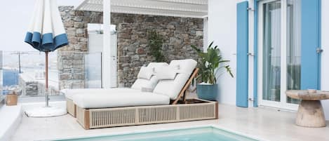 A poolside area with a lounge chair, a potted plant, and a stone wall.