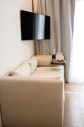 A modern living room with a beige sofa, a flat-screen TV mounted on the wall, and a small table with a bottle of champagne and glasses. - Numi Boutique Hotel Mykonos (Mykonos)