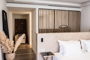 A modern hotel room with a minimalist design, featuring a sofa, a small side table, a decorative vase, and a wooden slat partition. - Numi Boutique Hotel Mykonos (Mykonos)
