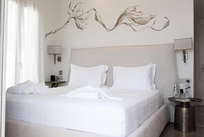 A hotel room with a large bed, two bedside lamps, a bedside table with a phone and a bottle, and a wall art piece. - Numi Boutique Hotel Mykonos (Mykonos)