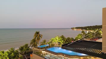 Piscina no terraço com vista para o mar, palmeiras e um edifício com fachada em azulejos.