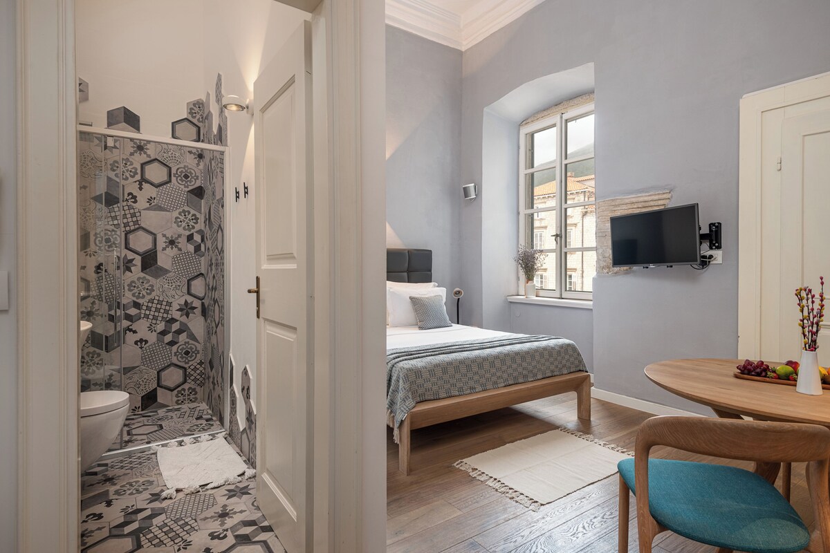 A bedroom with a bed, a bedside table, a TV, and a window.