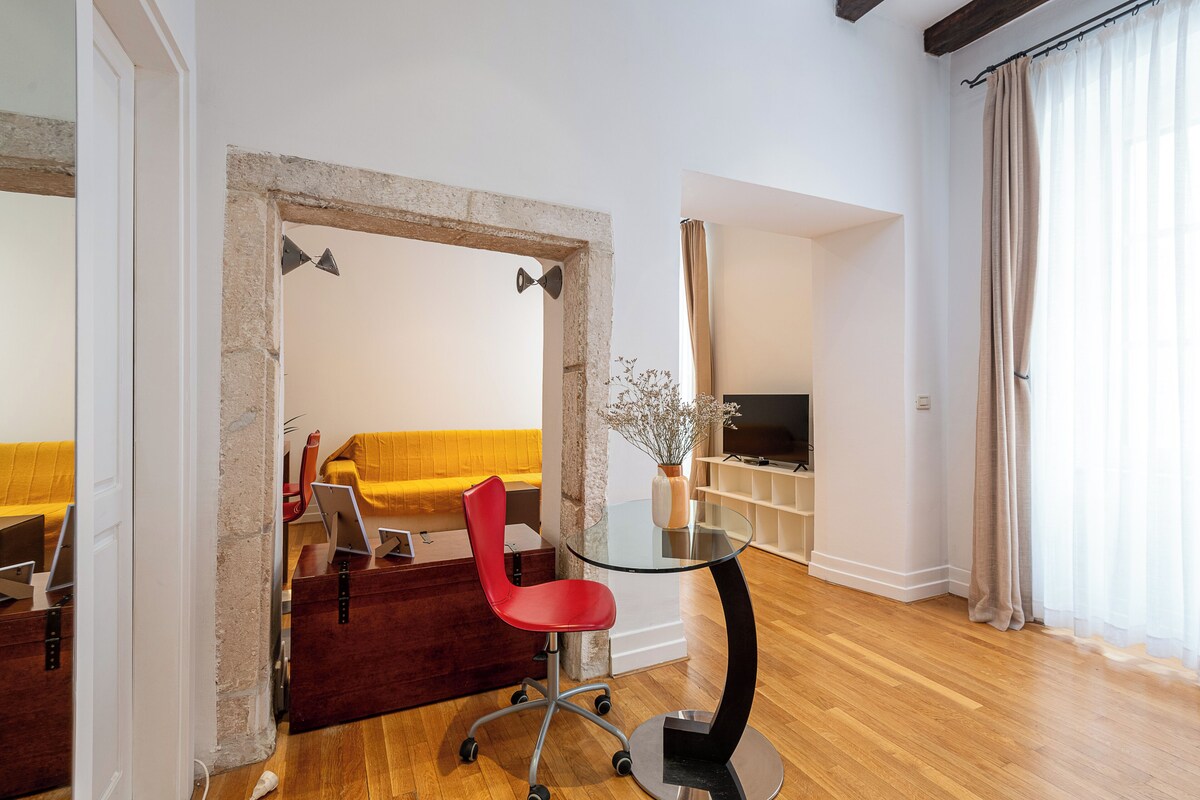 A modern living room with a glass table, red chair, wooden floor, and a yellow sofa.