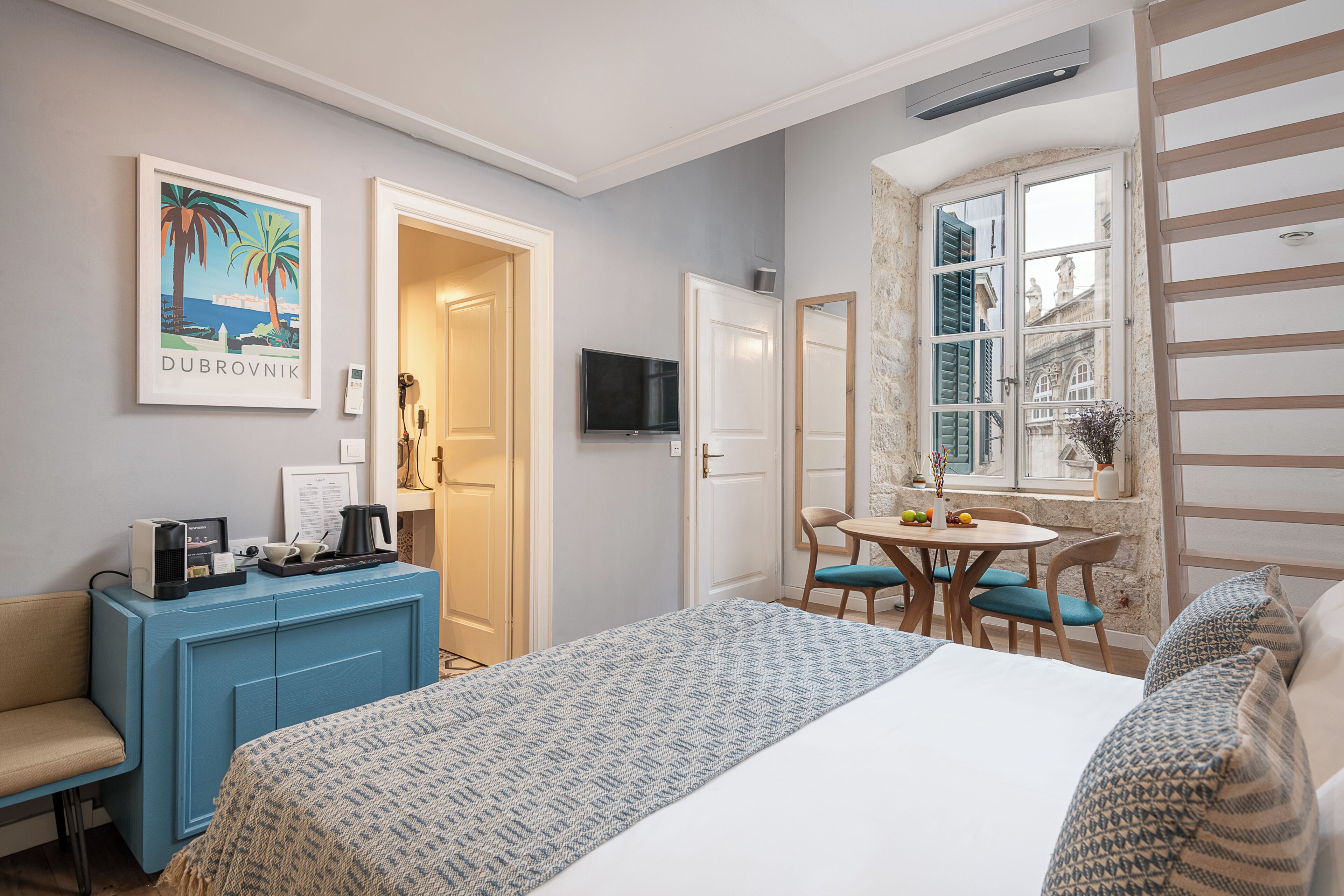 Ein Hotelzimmer mit Bett, Schreibtisch, Stuhl, kleinem Tisch, Fernseher und Fenster mit Aussicht.