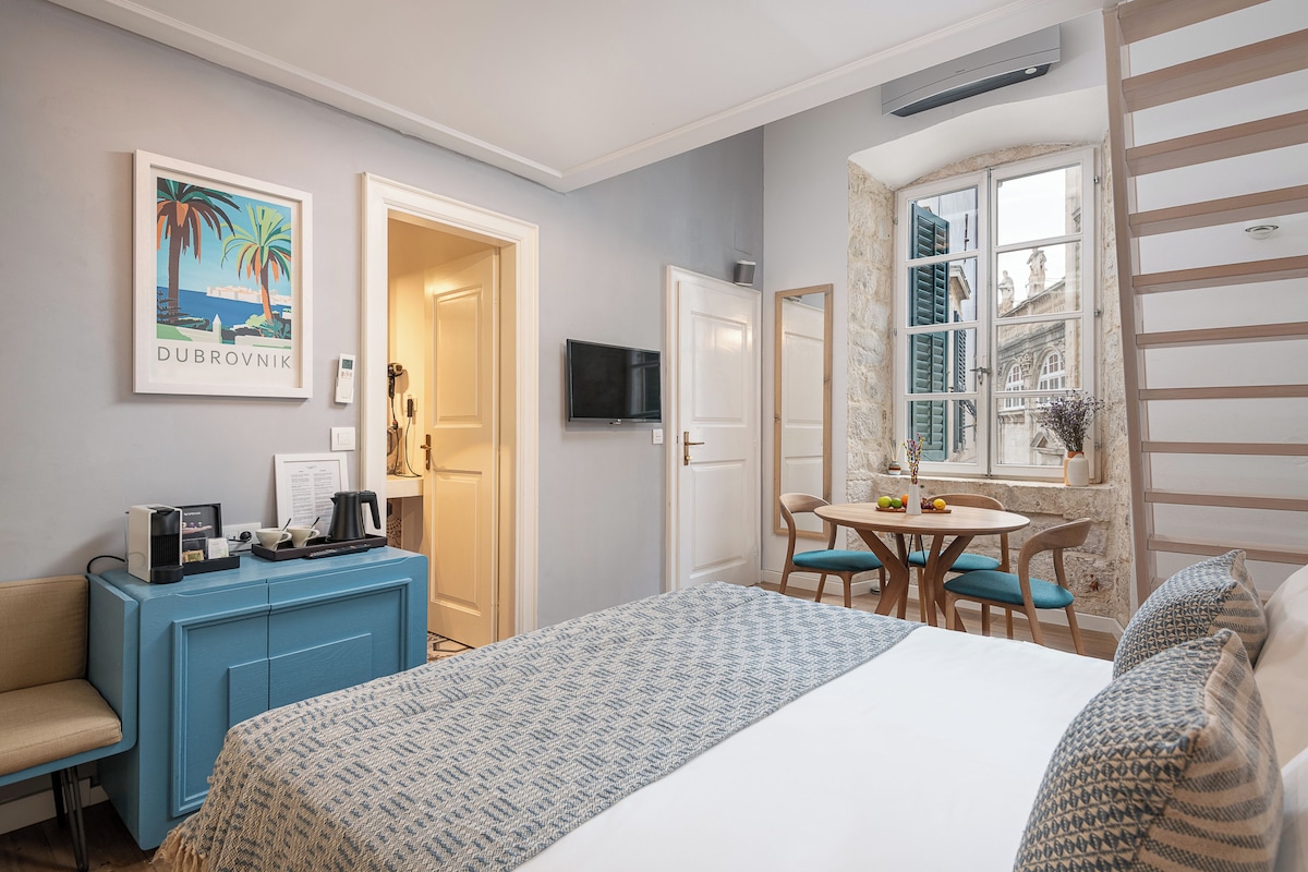 A hotel room with a bed, a desk, a chair, a small table, a TV, and a window with a view.