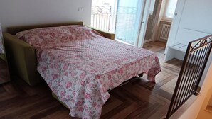 Un dormitorio con cama, suelo de madera, un balcón y una puerta que da a otra habitación.