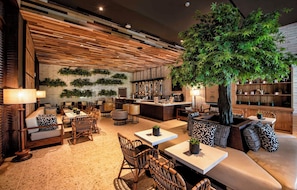 A modern lounge area with seating, a bar, and a large artificial tree. - Lopesan Splash Cove Resort, Spa & Casino (Punta Cana)
