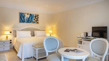 Une chambre d’hôtel avec un lit, deux chaises, une petite table, un téléviseur et un tableau au mur.