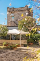 A courtyard with a stone building, a white canopy, potted plants, and hanging light fixtures.