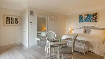 Une chambre d’hôtel comprenant un lit, une table à manger, deux chaises, une petite table avec une lampe et des œuvres d’art accrochées aux murs.