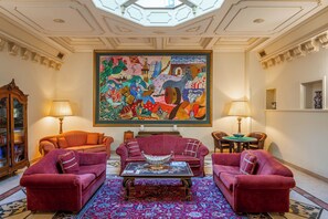 A room with a large colorful painting, two red sofas, a coffee table, and a chandelier. - San Giorgio Resort & Spa (Galatina)
