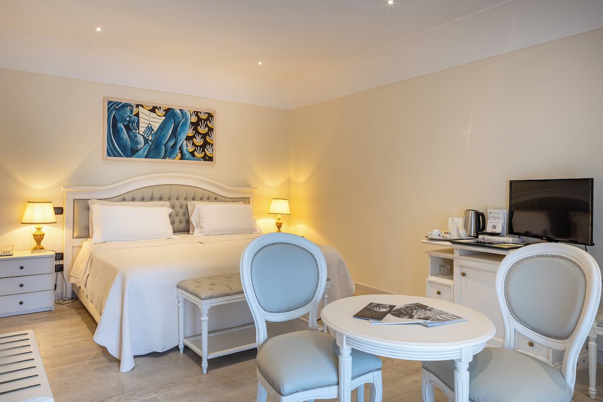 A hotel room with a bed, two chairs, a small table, a TV, and a painting on the wall.