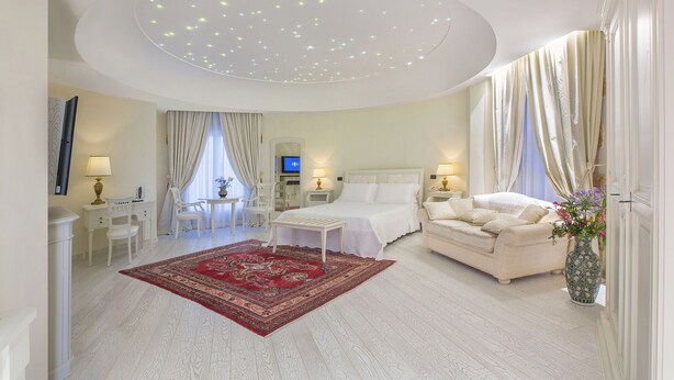 Une chambre d’hôtel avec un grand lit, un canapé, un bureau avec une chaise, une télévision et un plafond équipé de luminaires.